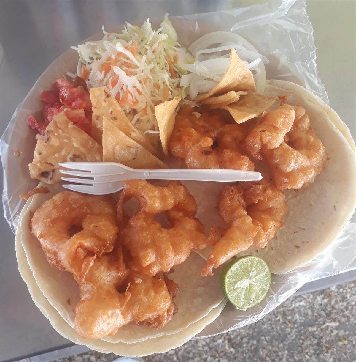 Taco de camarón capeado sobre tortilla con col, jitomate y limón