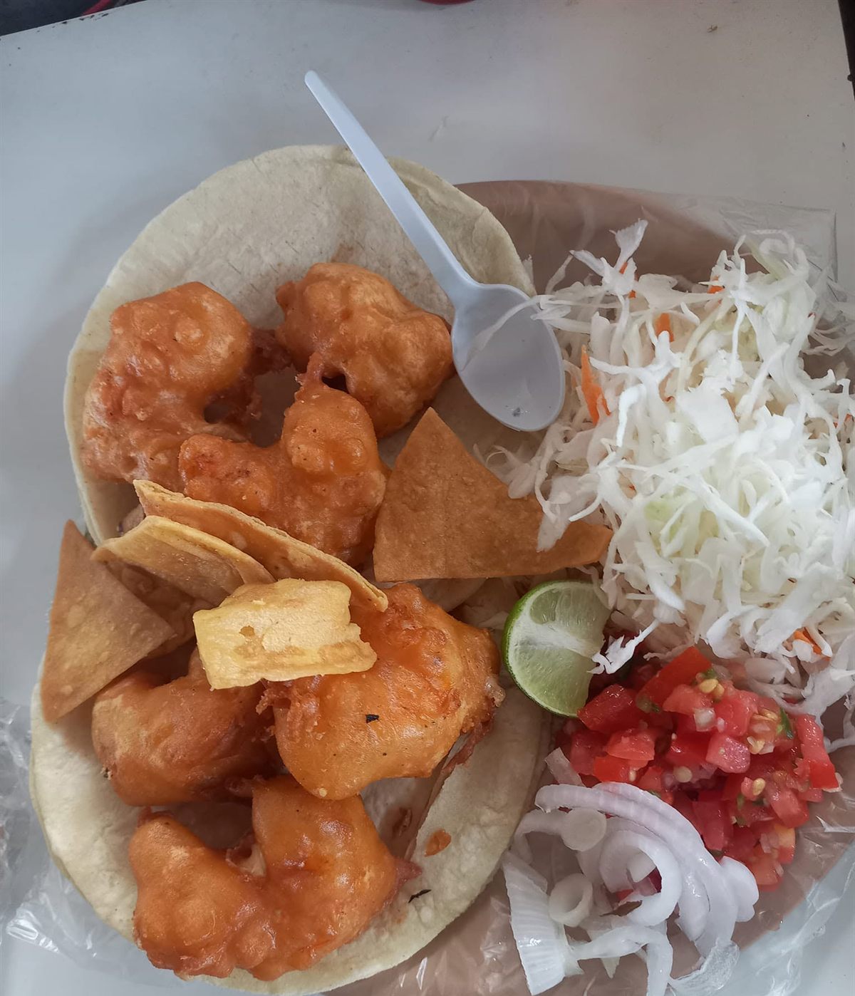Camarones capeados sobre tortilla con totopos, col, jitomate y limón
